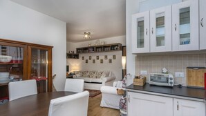 A compact kitchen with white cabinets, a dining table, and a sofa. - GuestHost - The window on the Raibl - Lovely APT with WiFi! x4 (Cave del Predil)