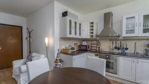 A modern kitchen with white cabinets, a stainless steel range hood, and a dining area with a round table. - GuestHost - The window on the Raibl - Lovely APT with WiFi! x4 (Cave del Predil)