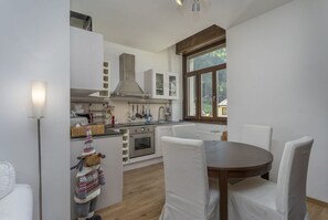 A modern kitchen with white cabinetry, a central island, and a dining area with white chairs.