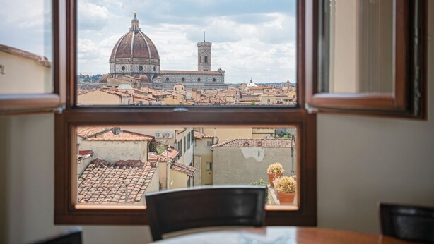 A window view of a historic building with a dome and tower, a tiled roof, and a chair with a potted plant. - GuestHost - San Marco Apartment with Panoramic View (Firenze)