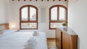 A bedroom with a bed, two arched windows, a radiator, and a view of a dome. - GuestHost - San Marco Apartment with Panoramic View (Firenze)