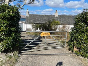 A gated entrance to The Old Ferryhouse with a sign, surrounded by greenery and a clear sky. - Historic  cottage in stunning coastal location (Port Appin)