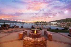 Une terrasse au bord du lac, dotée d’un foyer extérieur, de sièges et de guirlandes lumineuses.