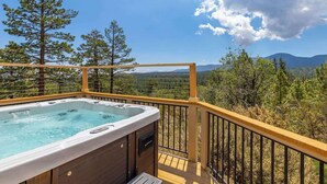 Een hottub op een terras met uitzicht op bomen en bergen.