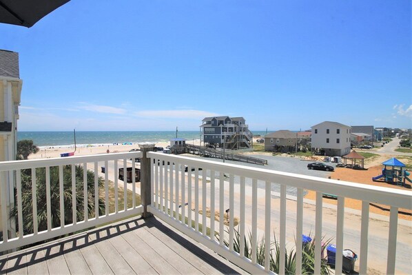 A balcony with a view of a beach, a lifeguard tower, and a playground.