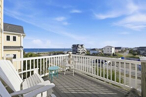 A wooden deck with white railings, a turquoise table, and two chairs.