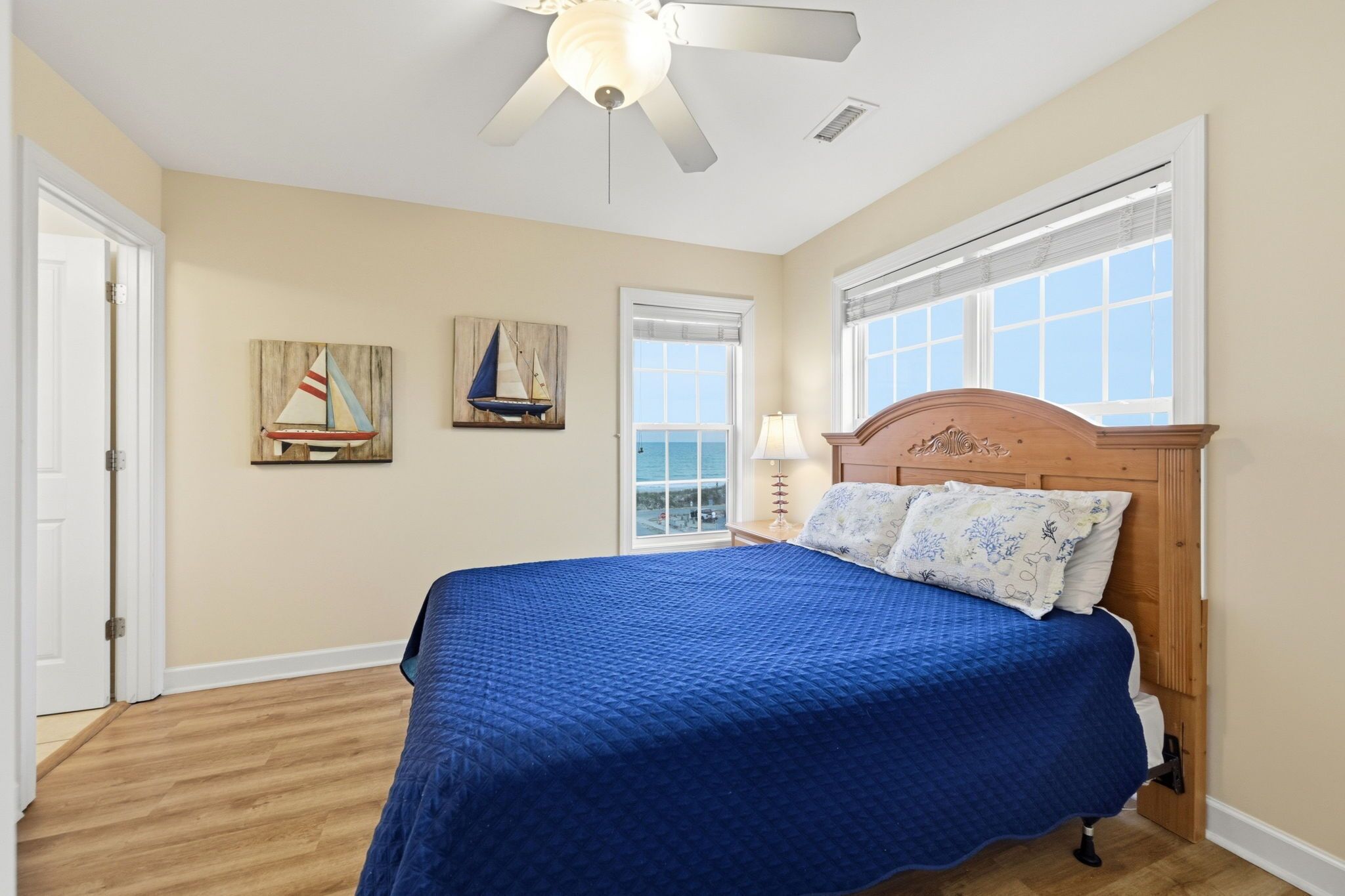 A bedroom with a bed, a ceiling fan, a window with a view, and two wall-mounted paintings.
