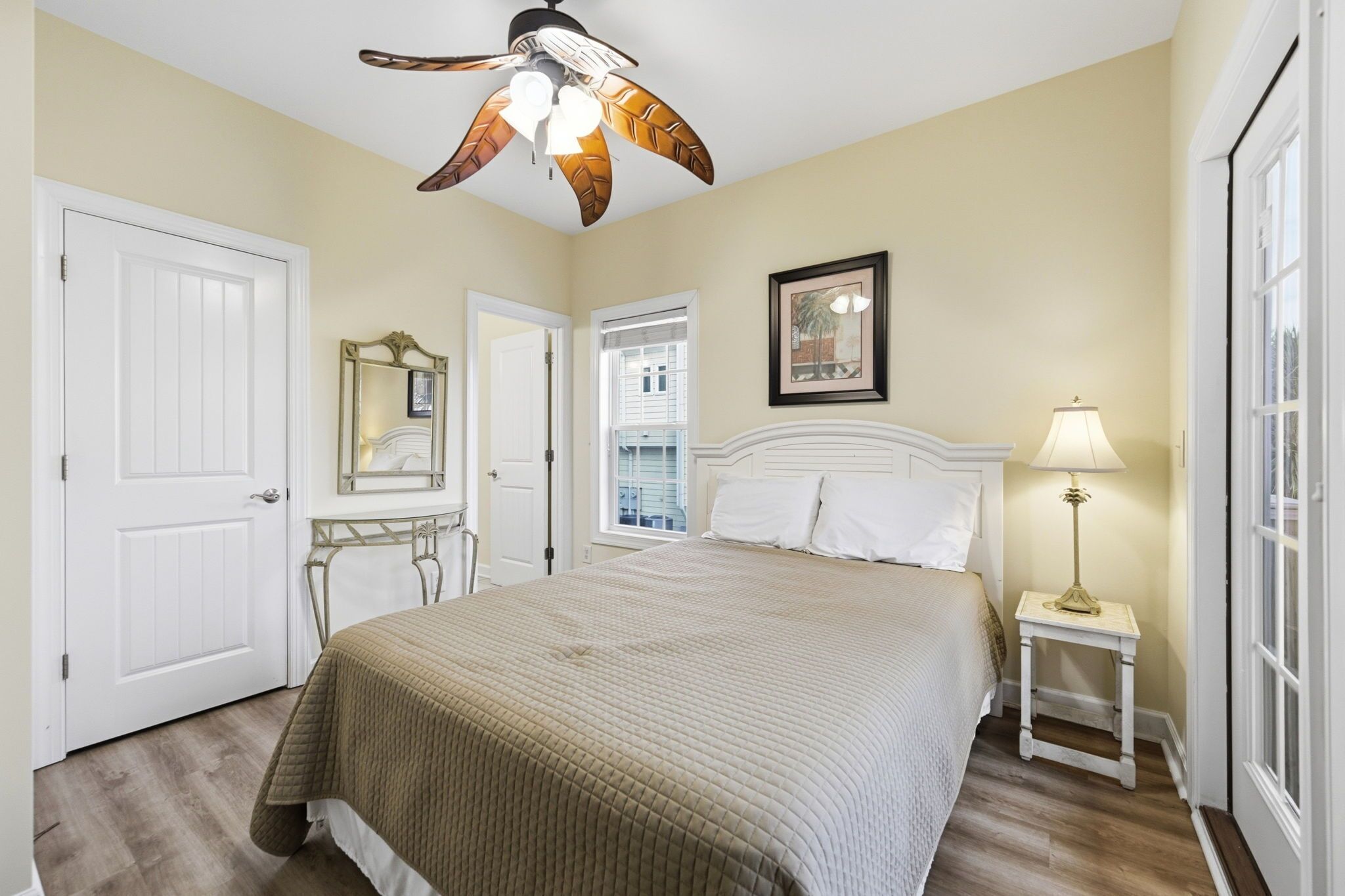 Une chambre à coucher avec un lit, un ventilateur de plafond, une table de chevet avec une lampe, une porte et une fenêtre.