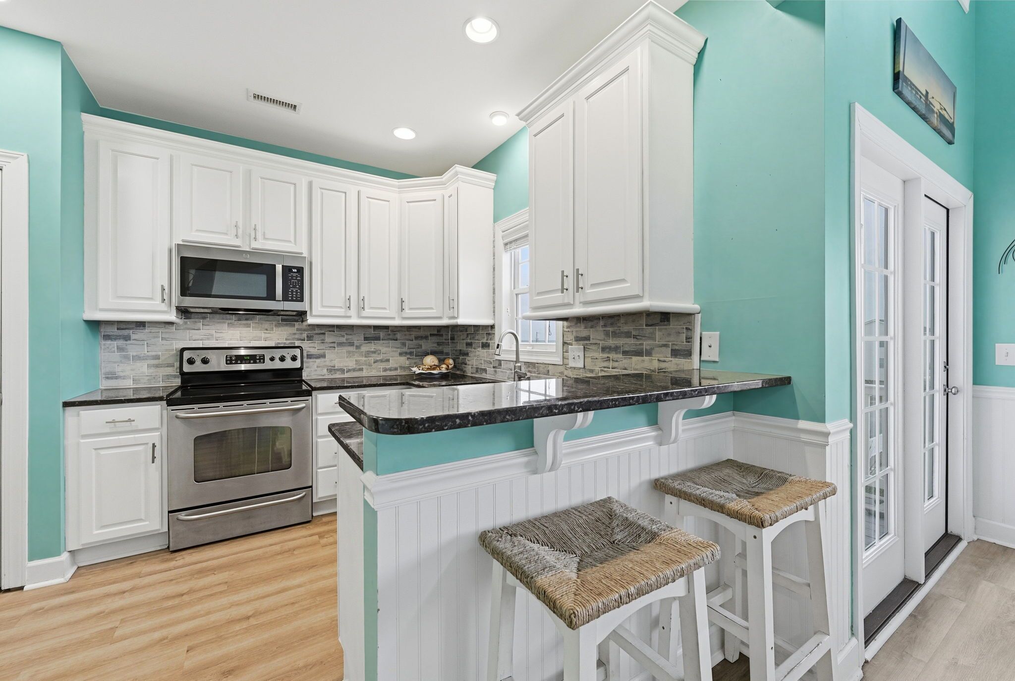 A kitchen with white cabinets, a granite countertop, a stainless steel oven, and a microwave.