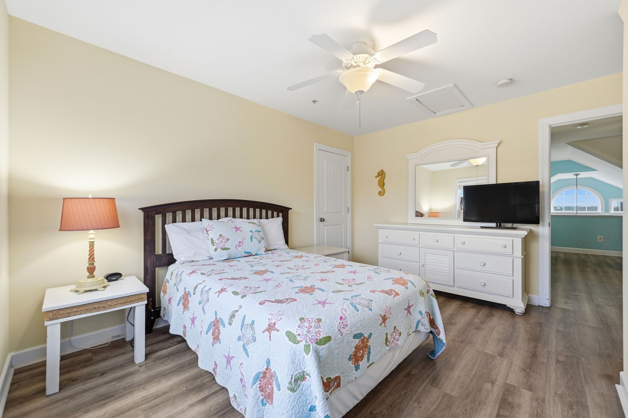 Une chambre à coucher comprenant un lit, une table de chevet, une lampe, une commode, un téléviseur et un ventilateur de plafond.