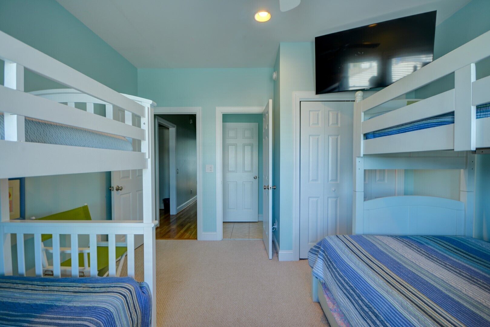 A room with bunk beds, a television, and a door leading to another room.