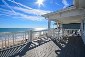 Een houten terras met een witte balustrade, uitkijkend op een strand.