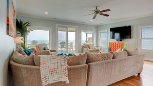 A spacious living room with a large sofa, a ceiling fan, and a television. - Sandy Paradise: An oceanfront, 6-bedroom retreat in Surf City, perfect for 20 guests! (Surf City)
