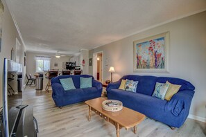 A living room with two blue sofas, a wooden coffee table, and a painting on the wall.