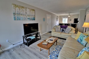 A living room with a flat-screen TV, a sofa, a coffee table, and a patterned rug.