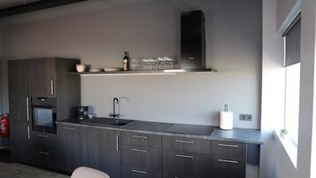 A modern kitchen with dark cabinetry, a built-in oven, a sink, and a window providing natural light.