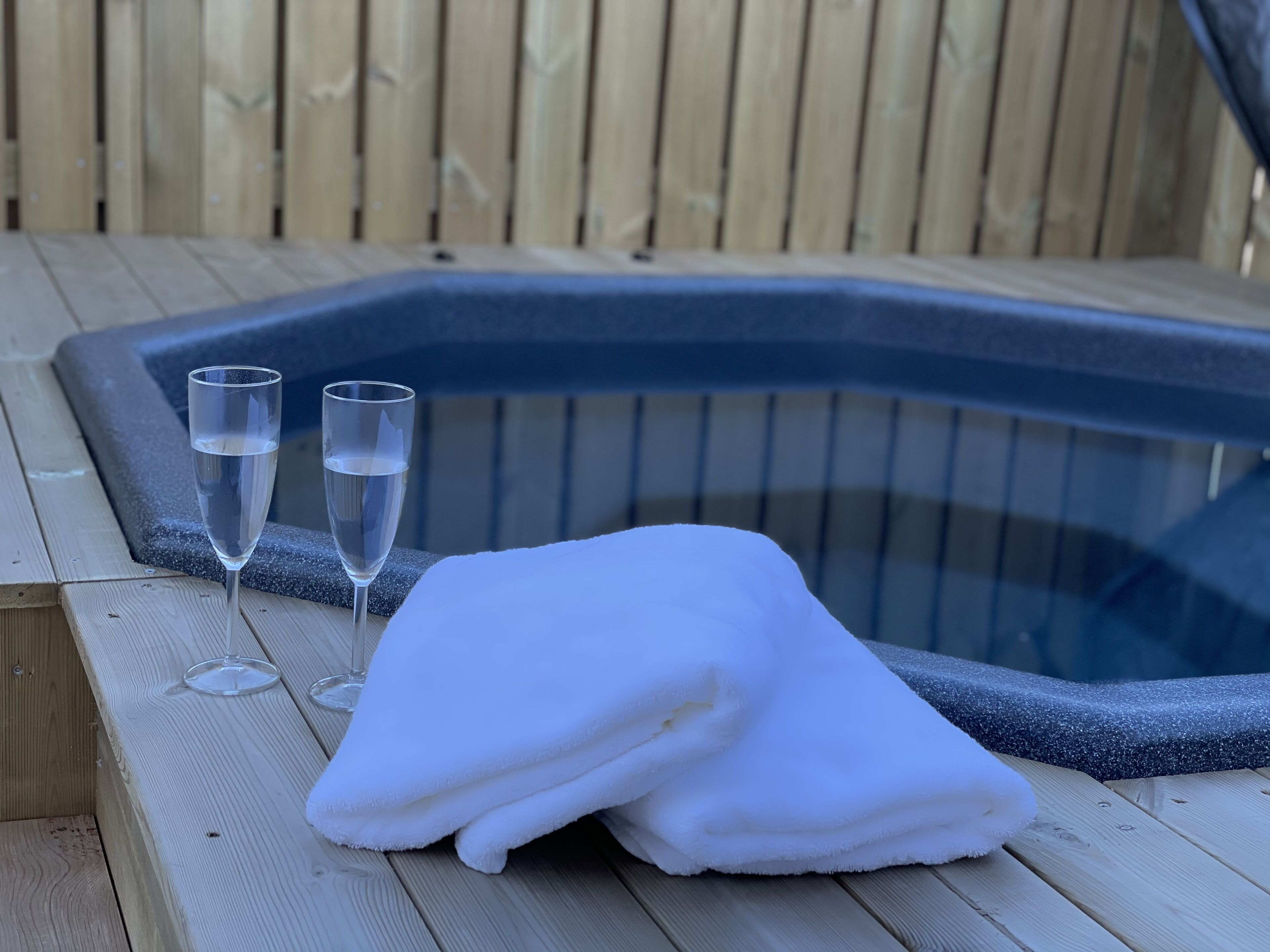 A wooden deck with a hot tub, two glasses of water, and a folded white towel.