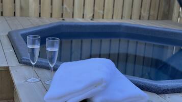 A wooden deck with a hot tub, two glasses of water, and a folded white towel.