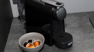 A black coffee machine with a cup holder and a bowl of coffee pods on a countertop.