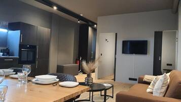 Uma sala de estar moderna com uma mesa de jantar de madeira posta para dois, um sofá e uma TV de tela plana na parede.