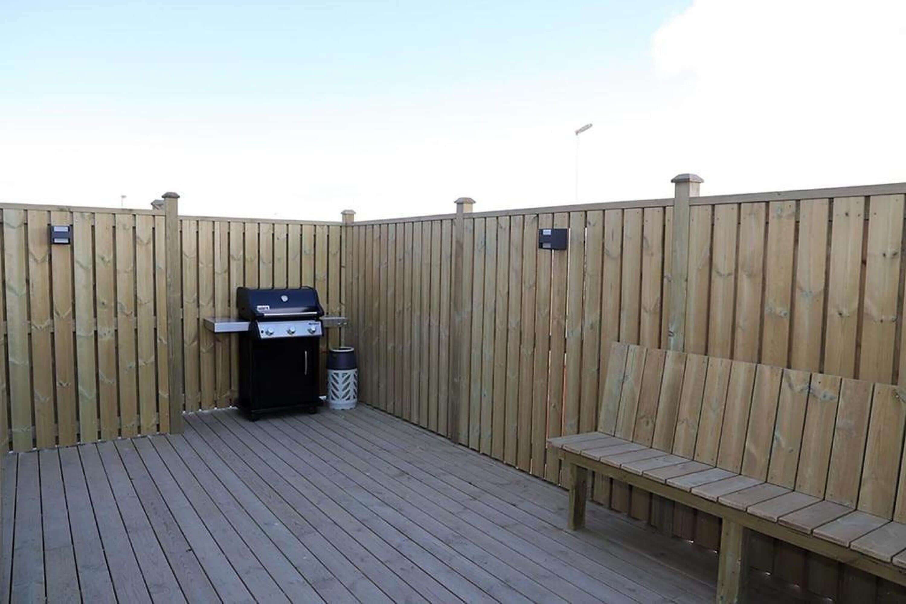 A wooden deck with a barbecue grill and a trash can.