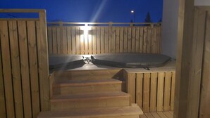A wooden outdoor hot tub with steps leading up to it, surrounded by a wooden fence.
