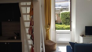 A compact living space with a kitchen area, a sofa, a TV, and a window with curtains. - Studio near the Château, the Old Port and the train station (Pornic)