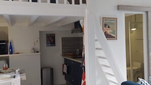 A compact living space with a kitchenette, a dining area, and a staircase leading to an upper level. - Studio near the Château, the Old Port and the train station (Pornic)