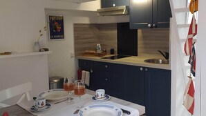A dining area with a table set for two, a kitchen with dark cabinets and a stainless steel sink, and a poster on the wall. - Studio near the Château, the Old Port and the train station (Pornic)