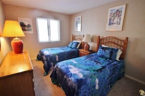 A bedroom with two beds, a wooden dresser, a window, and wall art.