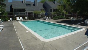 Ein rechteckiger Swimmingpool mit einer gefliesten Liegefläche, umgeben von Liegestühlen und einem Zaun.