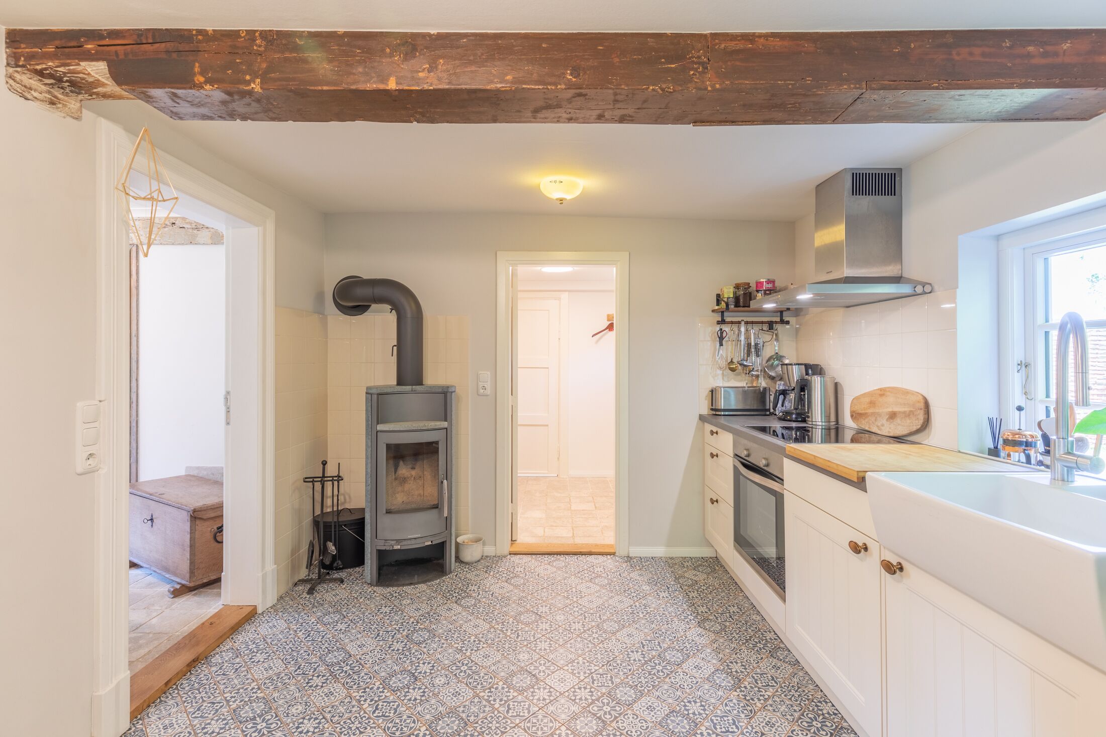 A kitchen with a wood-burning stove, white cabinets, a window, and a tiled floor.