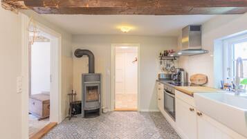 A kitchen with a wood-burning stove, white cabinets, a window, and a tiled floor.