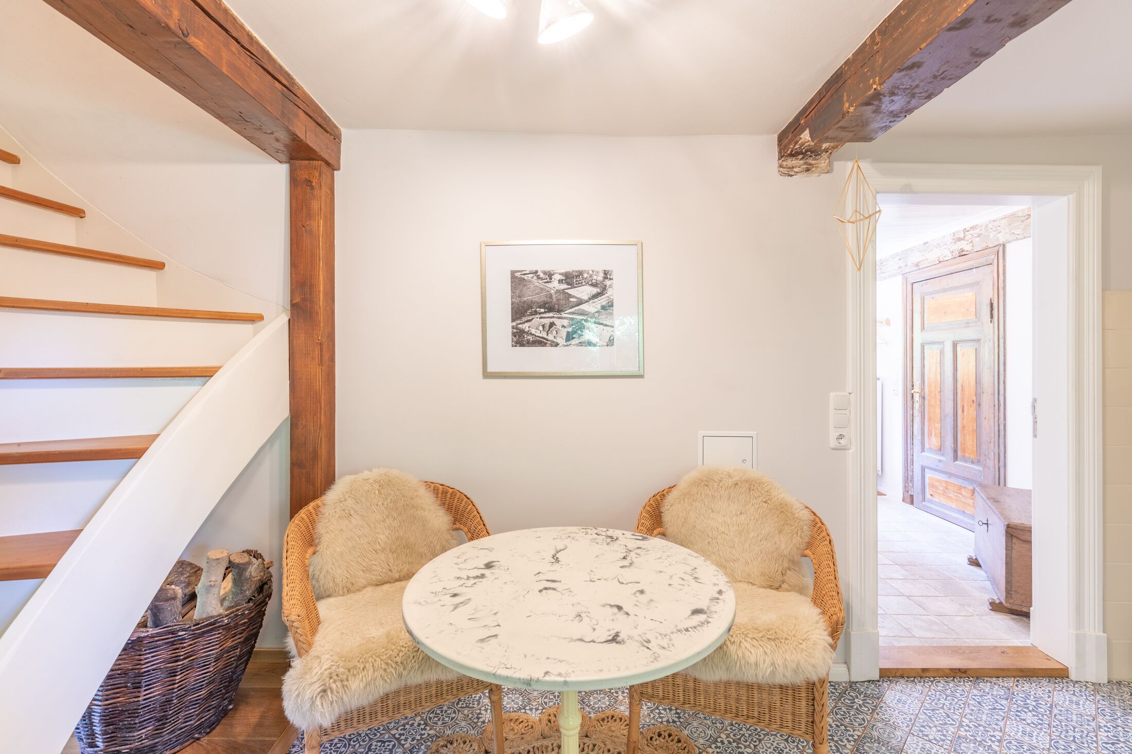 A room with a wooden staircase, a round table with chairs, a wicker basket, and a framed picture on the wall.