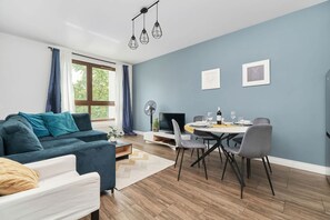 A modern living room with a sofa, dining table, and chairs, a TV, and a fan.