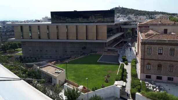 A modern building with a flat roof, a large open courtyard, and a view of a hillside in the background. - Check Point - Museum (Athens)