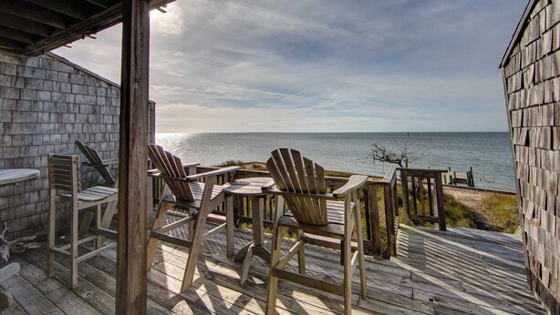 A wooden deck with Adirondack chairs overlooking a body of water.