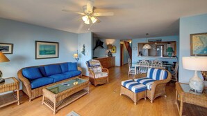 A living room with a blue sofa, wicker furniture, a ceiling fan, and a dining area with a table and chairs.