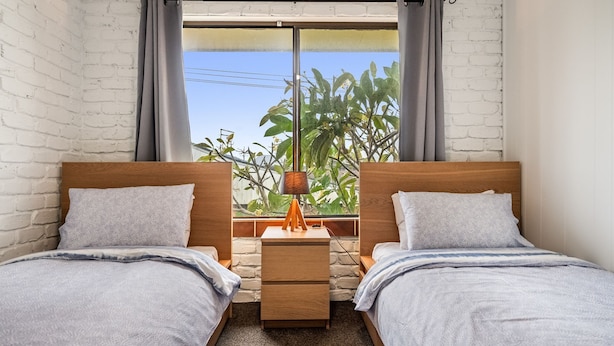 Une chambre avec deux lits, une table de chevet, une lampe et une fenêtre donnant sur un paysage verdoyant.