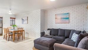 Un salon avec un mur en briques blanches, un canapé gris, une table à manger en bois et des chaises.