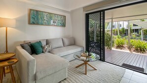 Een moderne woonkamer met een bank, een glazen salontafel en een uitzicht door een glazen deur op een terras.