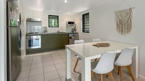 Een moderne keuken met een eethoek, met een witte tafel, stoelen en een macramé wanddecoratie.