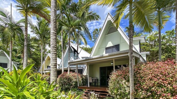 Een resort met meerdere bungalows, omgeven door weelderige begroeiing en palmbomen.