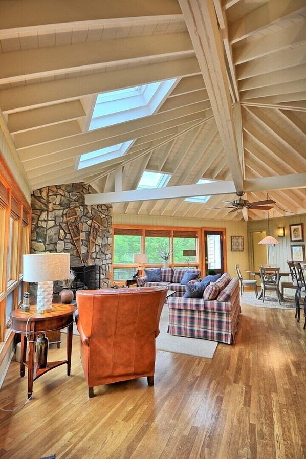 A spacious living area with a stone fireplace, wooden ceiling beams, and a large window.