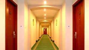 A hotel hallway with a green carpet, wooden doors, and a red door at the end. - Greentree Inn Beijing Tongzhou Tuqiao Subway Station Express Hotel (Tongzhou)