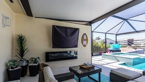 A modern living room with a flat-screen TV, comfortable seating, potted plants, and a view of a pool and buildings. - Welcome to your own private resort-style living (Marco Island)