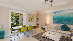 A modern living room with a dining area, a ceiling fan, a large painting, and a view of the outdoors. - Welcome to your own private resort-style living (Marco Island)