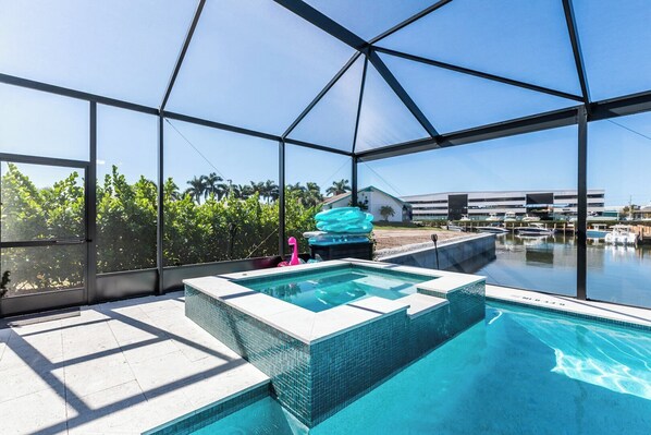 A swimming pool with a glass enclosure, surrounded by a patio area with a view of a marina and palm trees.