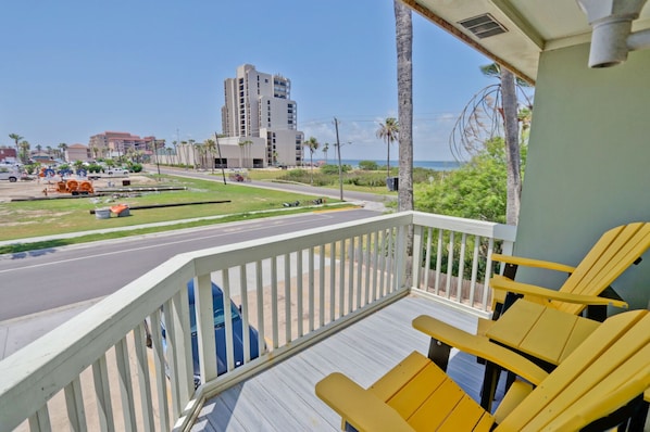 A balcony with yellow chairs, a view of a road with vehicles, and a tall building in the background.