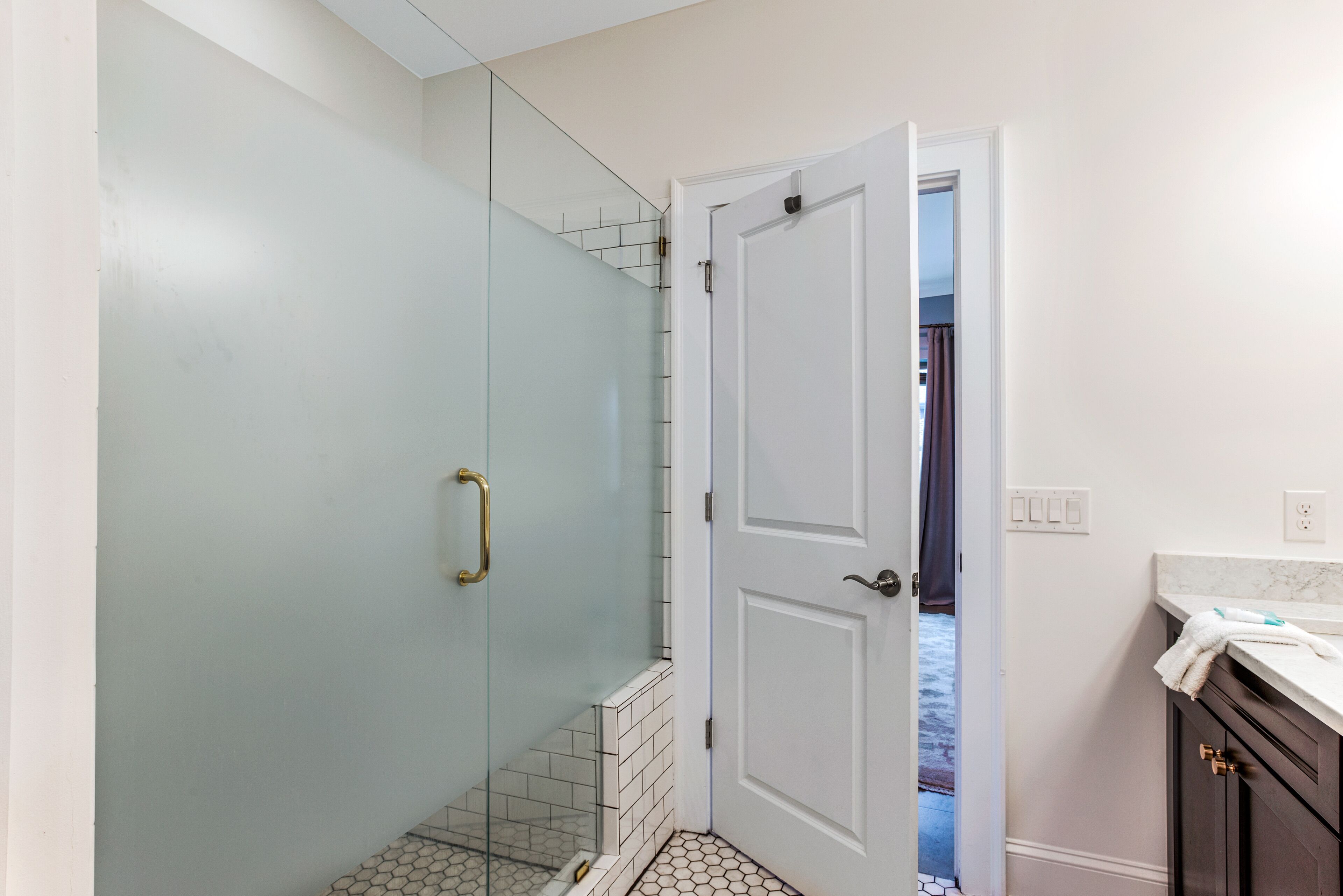 A bathroom with a glass shower enclosure, a white door, and a tiled floor.
